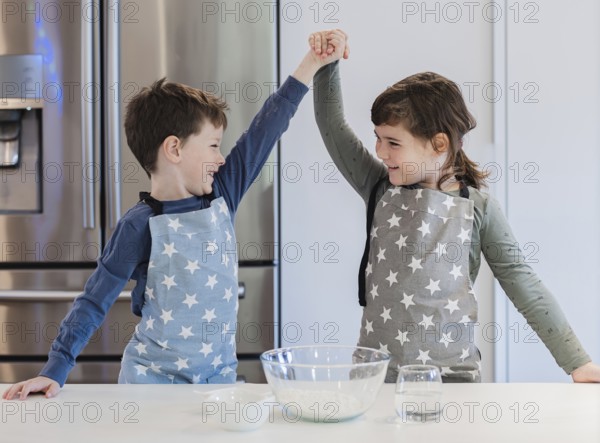 Two young siblings in star patterned aprons enthusiastically raise their hands in celebration while