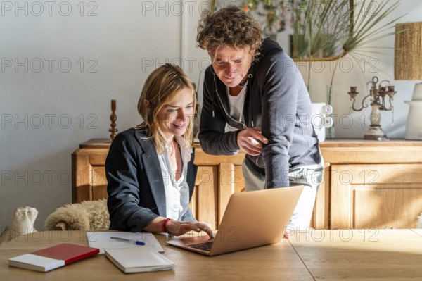 A couple works together at a home office, focused on a laptop The room is cozy, with natural