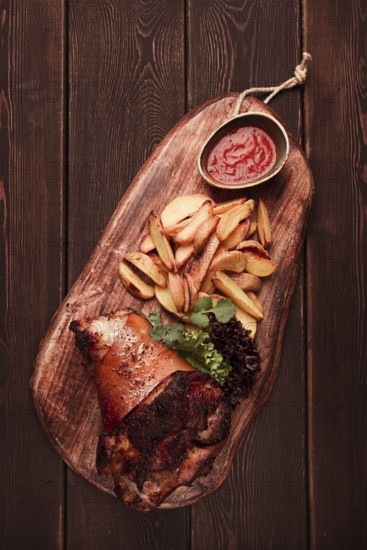 Pork knuckle, in soy-honey sauce, with fried potatoes, on a wooden chopping board, homemade, no