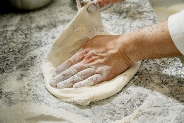 Cropped unrecognizable person kneading fresh pizza dough on a flour-dusted marble countertop,