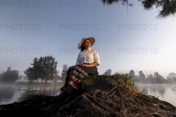 A woman in traditional attire enjoys a peaceful moment by the water in Xochimilco, Mexico.