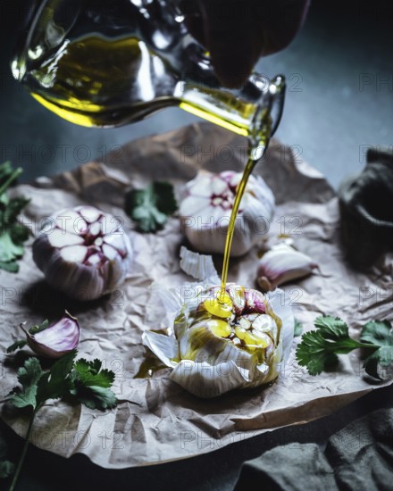 Close-up of garlic bulbs drizzled with olive oil, surrounded by fresh herbs on crumpled parchment