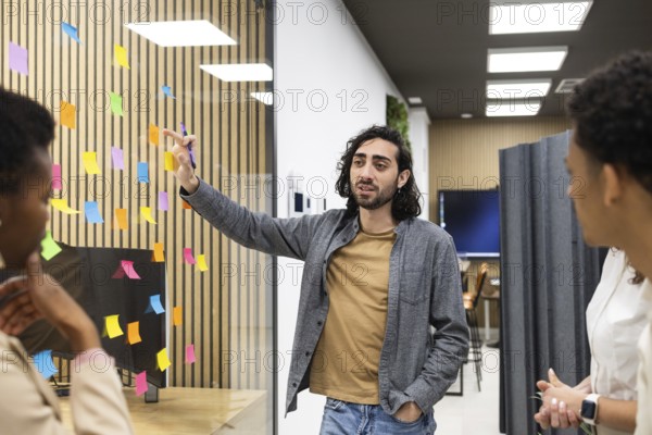 Professionals engage in a brainstorming session in a modern office space. A man gestures towards