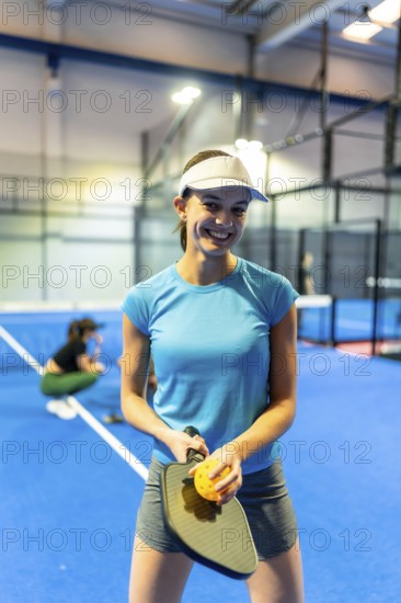 Young woman smiling and holding a pickleball paddle with a perforated ball, standing on a bright