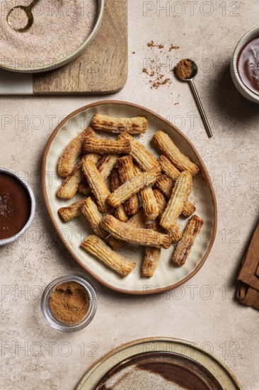 Top view of a ceramic plate filled with sugary churros next to bowls of chocolate sauce and
