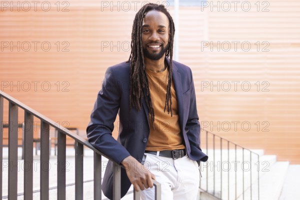 Cuban business man with long hair wearing a blazer and casual attire, leaning against a staircase