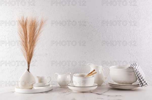 A minimalist interior design featuring elegant white tableware and a decorative vase with dried