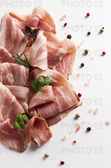 Raw bacon, sliced, with micro greenery and spices, on a white background, close-up