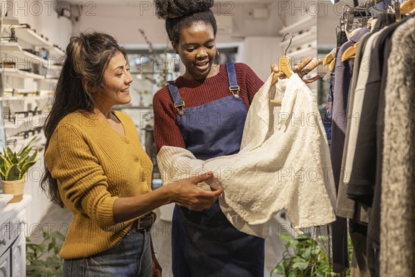 A boutique employee assists a customer in choosing clothing. They are smiling and engaged while