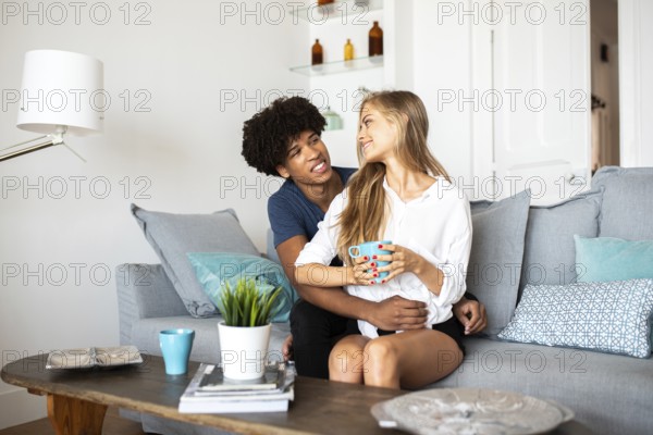 A couple sits together on a comfortable couch, sharing a warm moment with coffee. The bright and