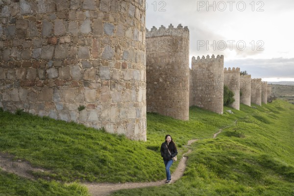 An Asian female tourist strolls along Avila's ancient medieval walls. The scene captures cultural