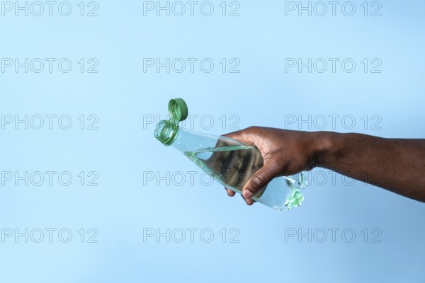 A close-up image of a hand holding a transparent water bottle with a green cap, set against a