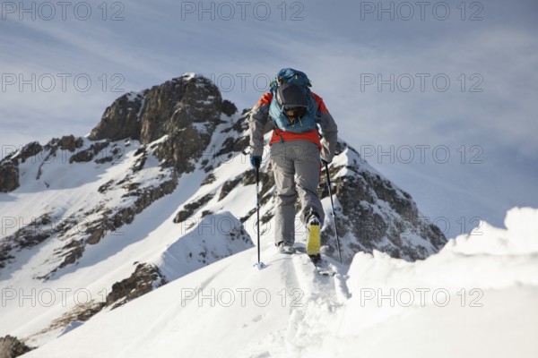 A skier in vibrant gear ascends a snowy peak, showcasing the thrill and challenge of ski touring