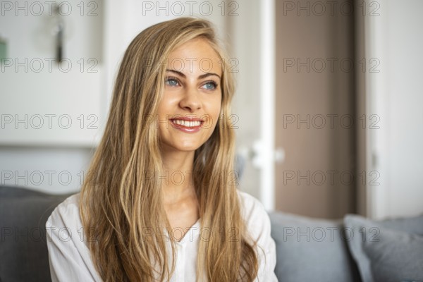 Portrait of a smiling woman with long blonde hair sitting in a bright, cozy room. She looks relaxed