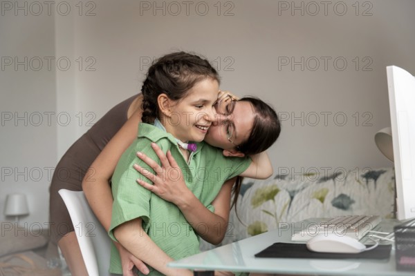 Young disabled girl with a tracheostomy, being embraced and kissed by sister while using desktop