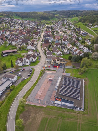 Roads cross a village with a building and neighbouring fields from an aerial perspective,