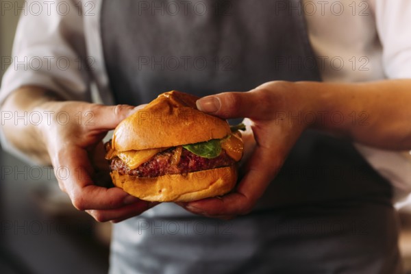 Close-up of an artisan burger presented by a chef. Brioche bun, juicy beef, and melted cheese take
