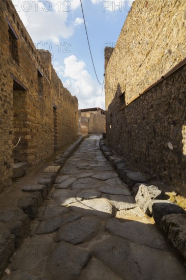 Long narrow street made of large grey smooth and worn lava stones with sidewalk plus remnants of