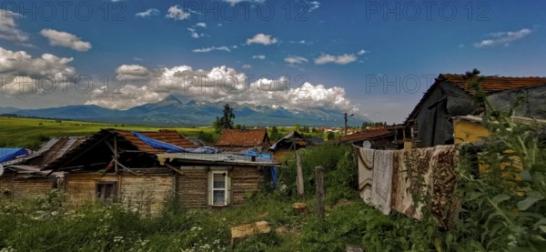 Rural scene with huts and mountains under a wide cloudy sky, atmospheric atmosphere, bright colors,