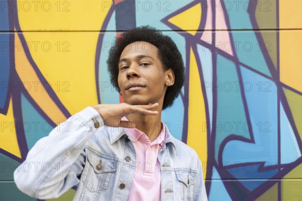 A confident non-binary person stands proudly in front of a vibrant graffiti mural. They wear a