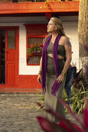 An elegant woman with tattoos, purple scarf and tight green dress walks down a vibrant and colorful
