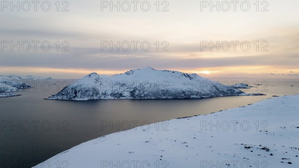A breathtaking aerial view captures a Nordic winter landscape with a tranquil snowy island