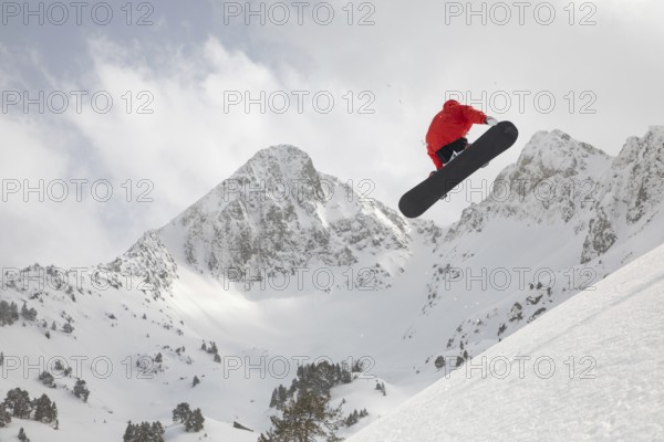 A snowboarder in vibrant gear catches air while performing a jump against a backdrop of majestic