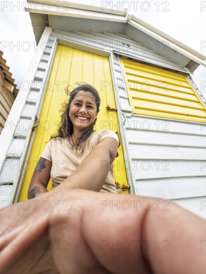 A woman smiles while leaning against a brightly painted yellow Brighton Bathing Box in Melbourne,