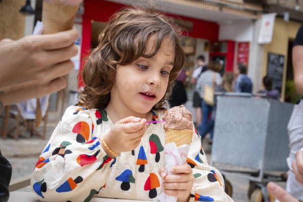A young girl delights in eating chocolate ice cream from a cone in a quaint village scene,