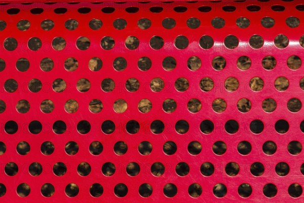Close-up of vibrant red painted metal sitting bench backrest with perforated round holes, Quebec,