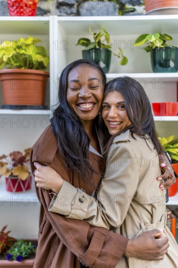 Two multi ethnic female friends are hugging each other with eyes closed in a plant shop,