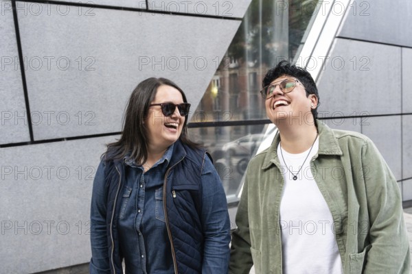 A happy lesbian couple enjoying a sunny day, laughing together outdoors in an urban setting. They
