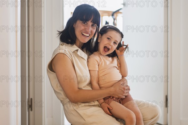 A joyful young mother lovingly embraces her playful toddler daughter in a bright home environment.
