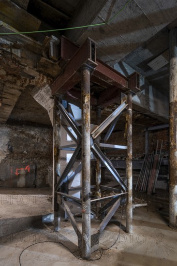 A metal support structure stands firm in a dimly lit construction site. Exposed beams, wooden
