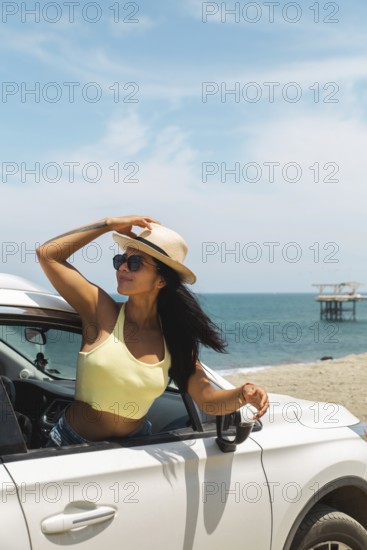 A young Latin woman in a yellow top and sunglasses enjoying the breeze and ocean view from a car at