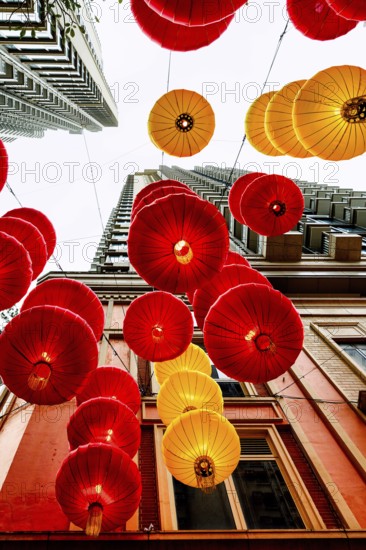 From below radiant red and yellow lanterns hang between skyscrapers in Hong Kong, celebrating