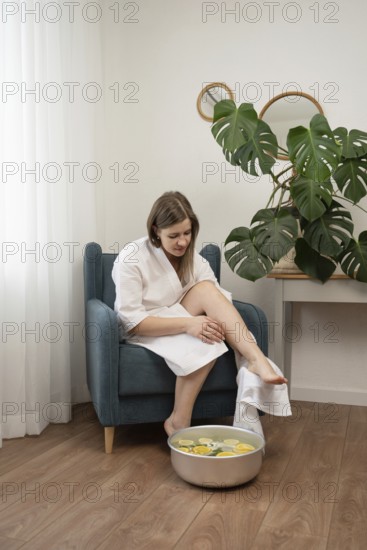 A woman in a white bathrobe enjoys a relaxing foot bath with citrus and flowers at home. The cozy