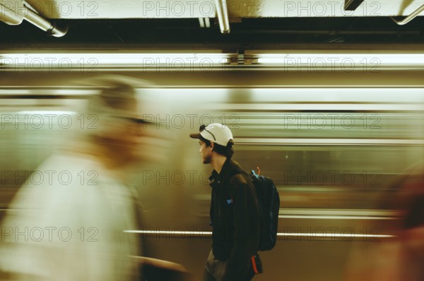 A man pauses in a bustling subway, surrounded by blurred commuters in New York. The scene captures