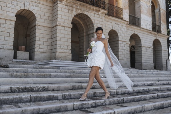 A beautiful bride in a white dress and veil gracefully descends the ancient stone steps of a