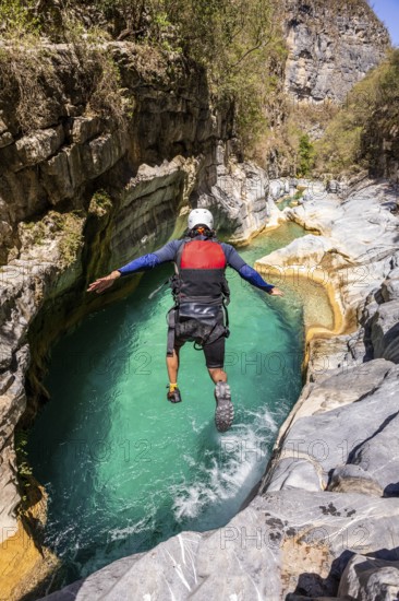 A canyoneer leaps into vibrant turquoise waters surrounded by rugged cliffs in Matacanes, Nuevo