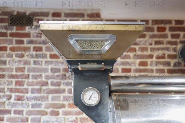 An industrial coffee roasting machine is showcased against a rustic brick wall. The machine holds