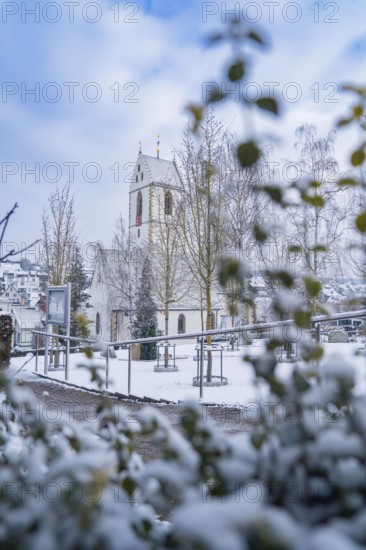 Snow-covered church with decorated tower behind trees and bushes, Aidlingen, Böblingen district,