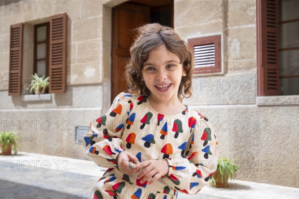 A joyful child, dressed in colorful attire, plays in the sunlit street of a quaint village,