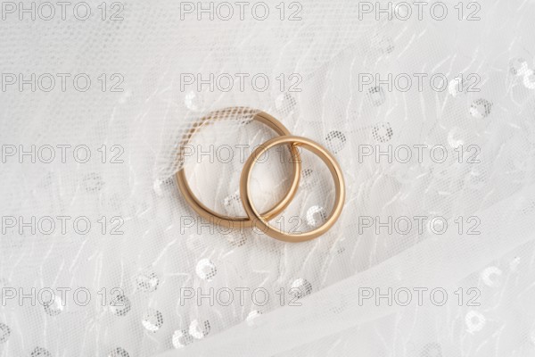 Close-up of two intertwined rose gold wedding rings atop a delicate white lace fabric, symbolizing