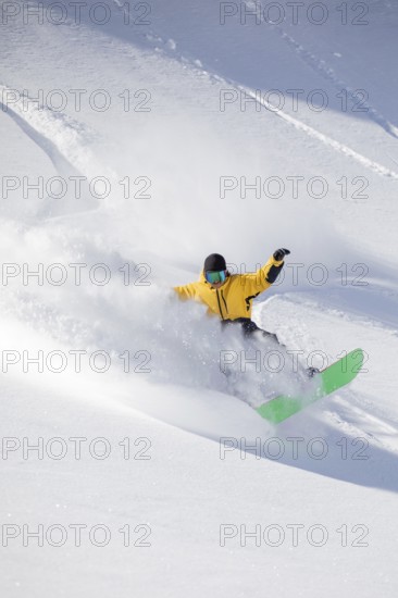 A snowboarder in a vibrant yellow jacket expertly carves through fresh powder on a snowy mountain