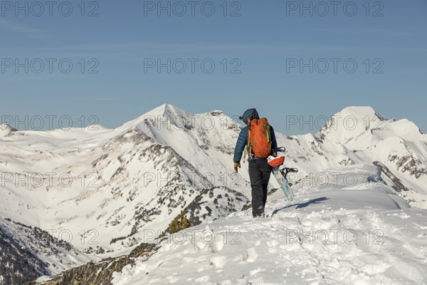 Back view of an unrecognizable person hiking up a snow-covered mountain with a snowboard. The