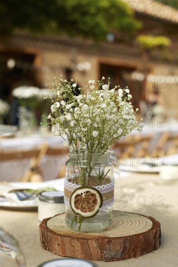 A rustic wedding table centerpiece featuring delicate white flowers in a mason jar adorned with