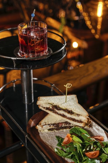 A gourmet club sandwich filled with tender veal cheeks, served alongside a fresh tomato and spinach