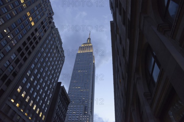 Low angle of the Empire State Building towers majestically between neighboring skyscrapers in