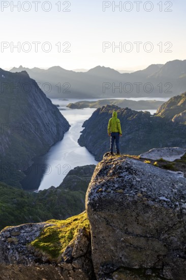 Mountaineer, young man standing on rocks and looking into the distance, at sunrise, fjord